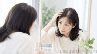 鏡を見ながら生え際を気にする女性。薄毛や抜け毛に悩む様子